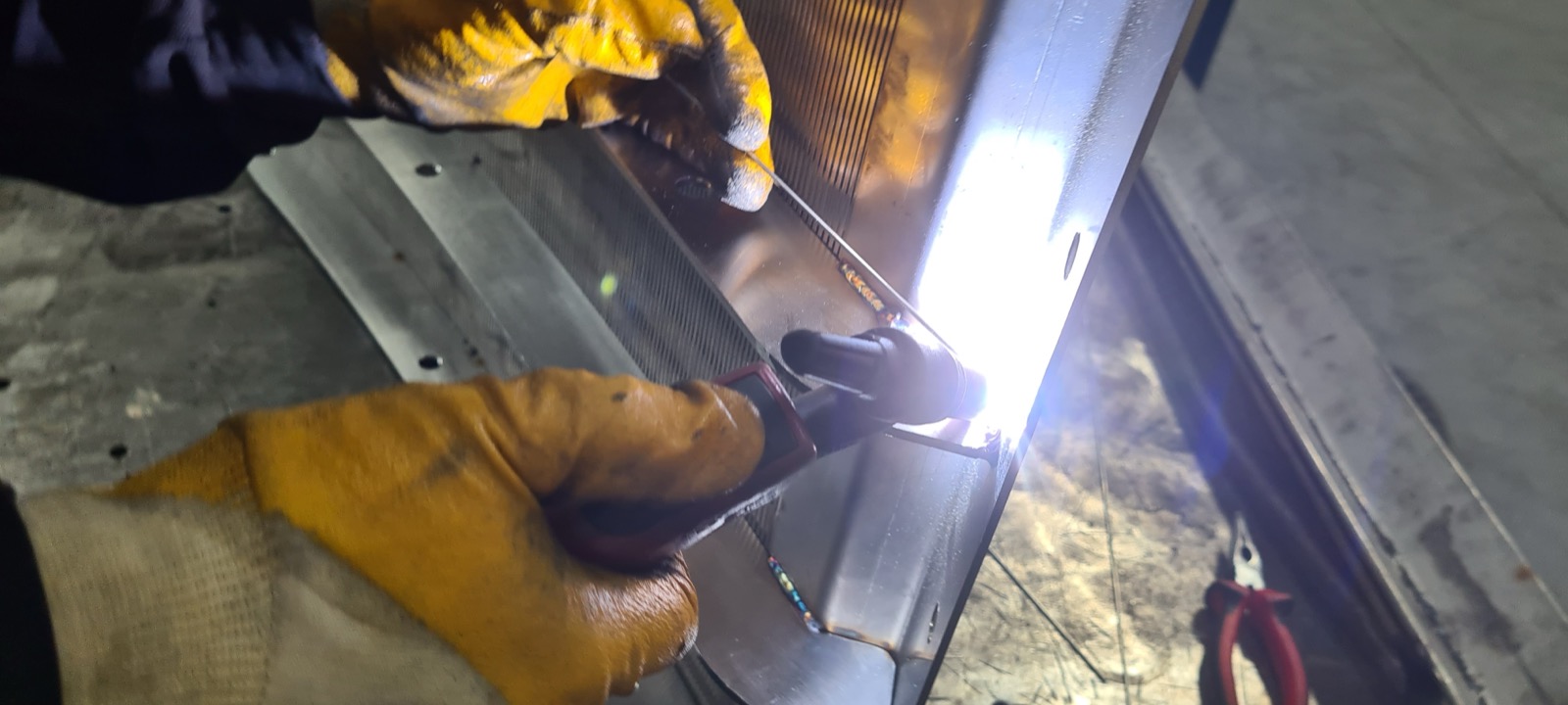 Skilled technician performing manual welding on a stainless steel wedge wire screen panel